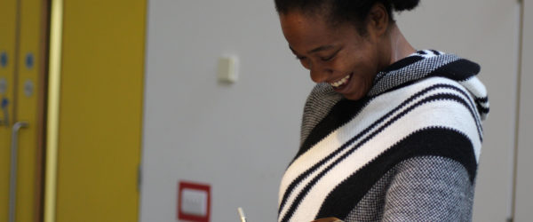 Photo of a black woman looking and smiling at a notepad while she takes notes in rehearsals.