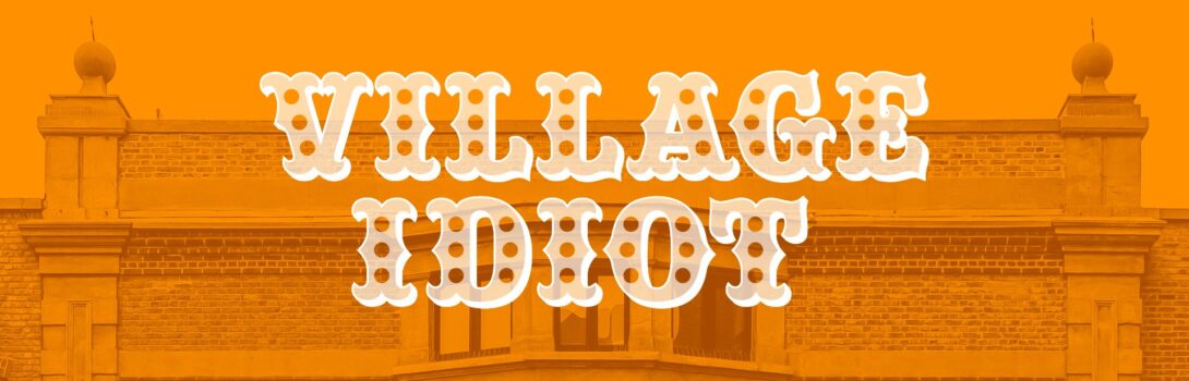 A photo of a grand building, like a town hall, is bathed beneath an orange colour, the words 'Village Idiot' written over the top in an old-fashioned white font.